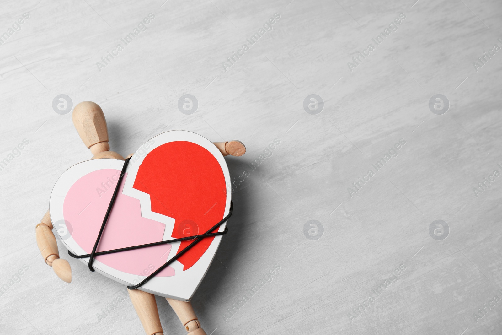 Photo of Wooden puppet with symbol of broken heart on gray background, space for text. Relationship problems