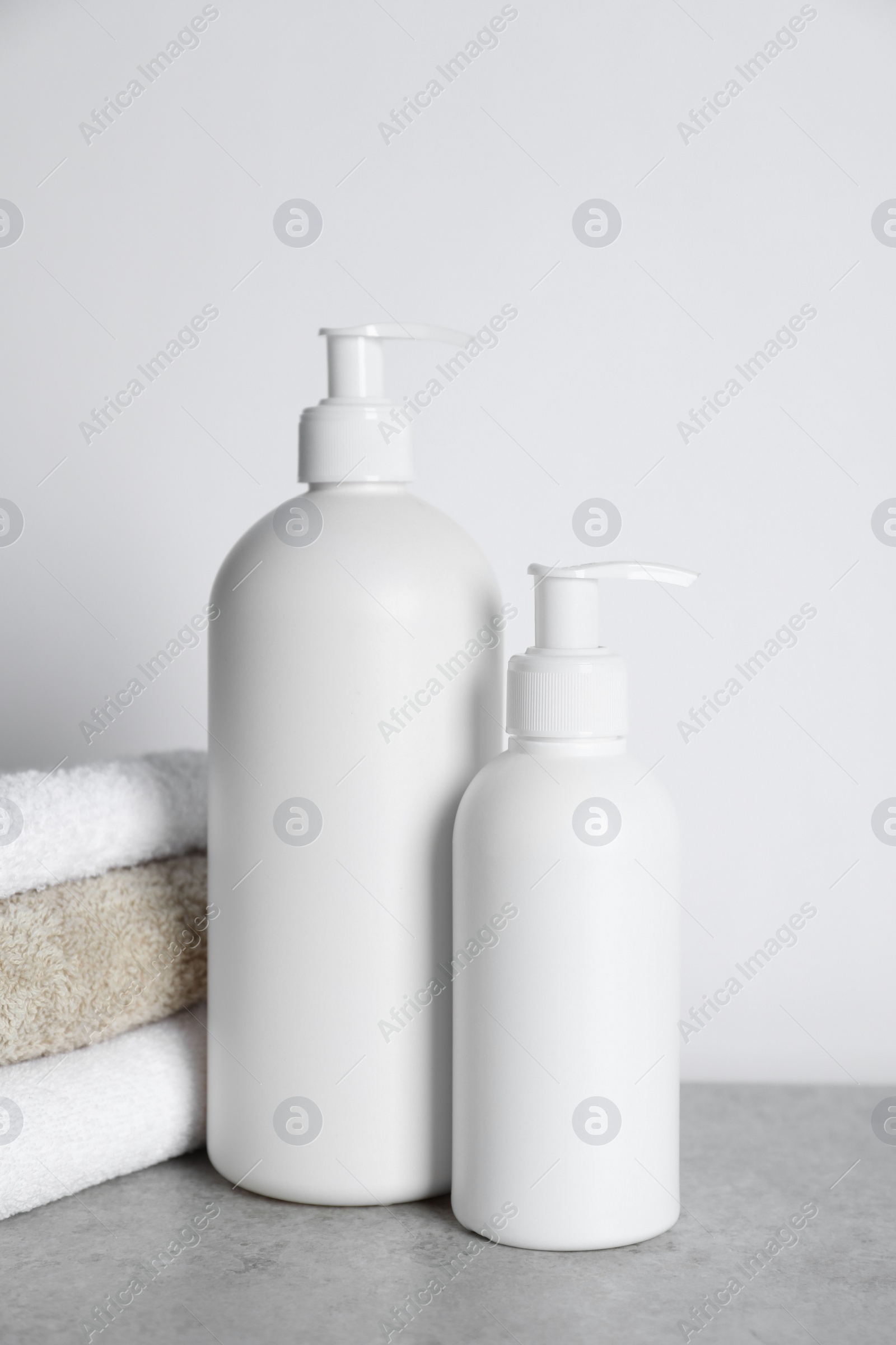 Photo of Bottles of cosmetic products and towels on grey table