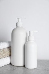 Bottles of cosmetic products and towels on grey table