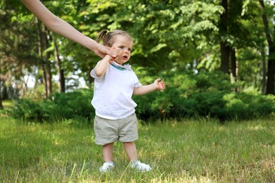 Photo of Mother supporting daughter while she learning to walk in park. Space for text