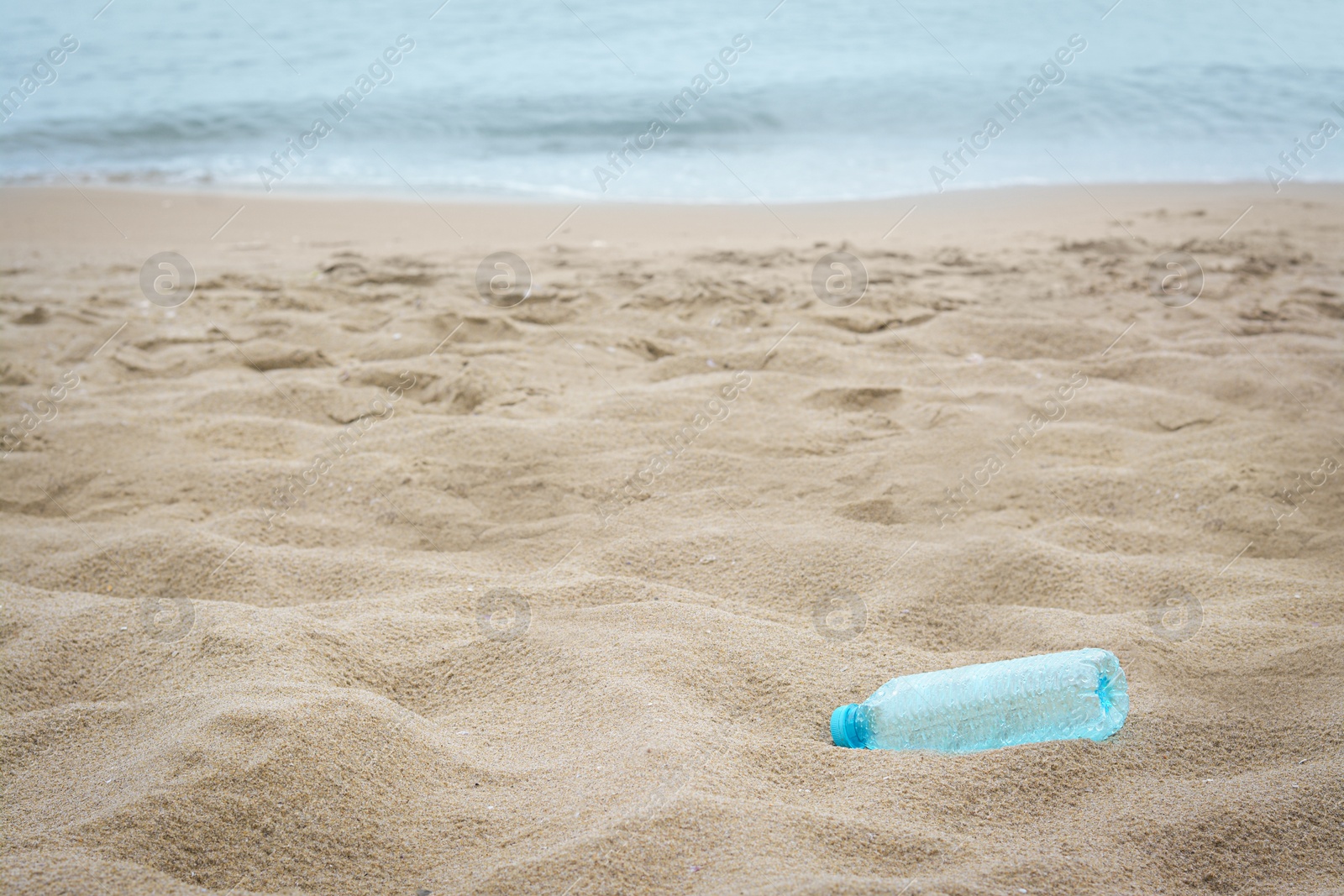 Photo of Plastic bottle on beach near sea, space for text. Recycling problem