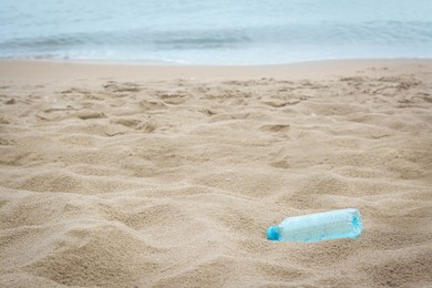 Photo of Plastic bottle on beach near sea, space for text. Recycling problem