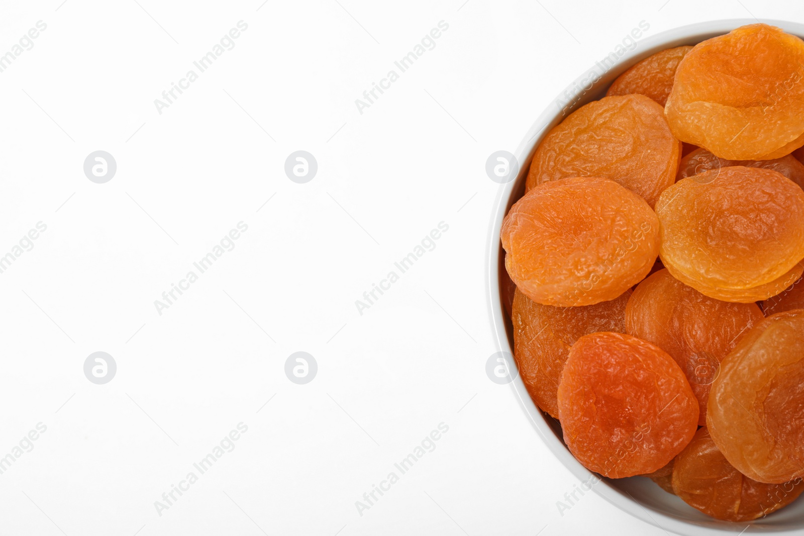Photo of Bowl of dried apricots on white background, top view with space for text. Healthy fruit