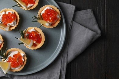 Delicious tartlets with red caviar and cream cheese served on wooden table, top view. Space for text