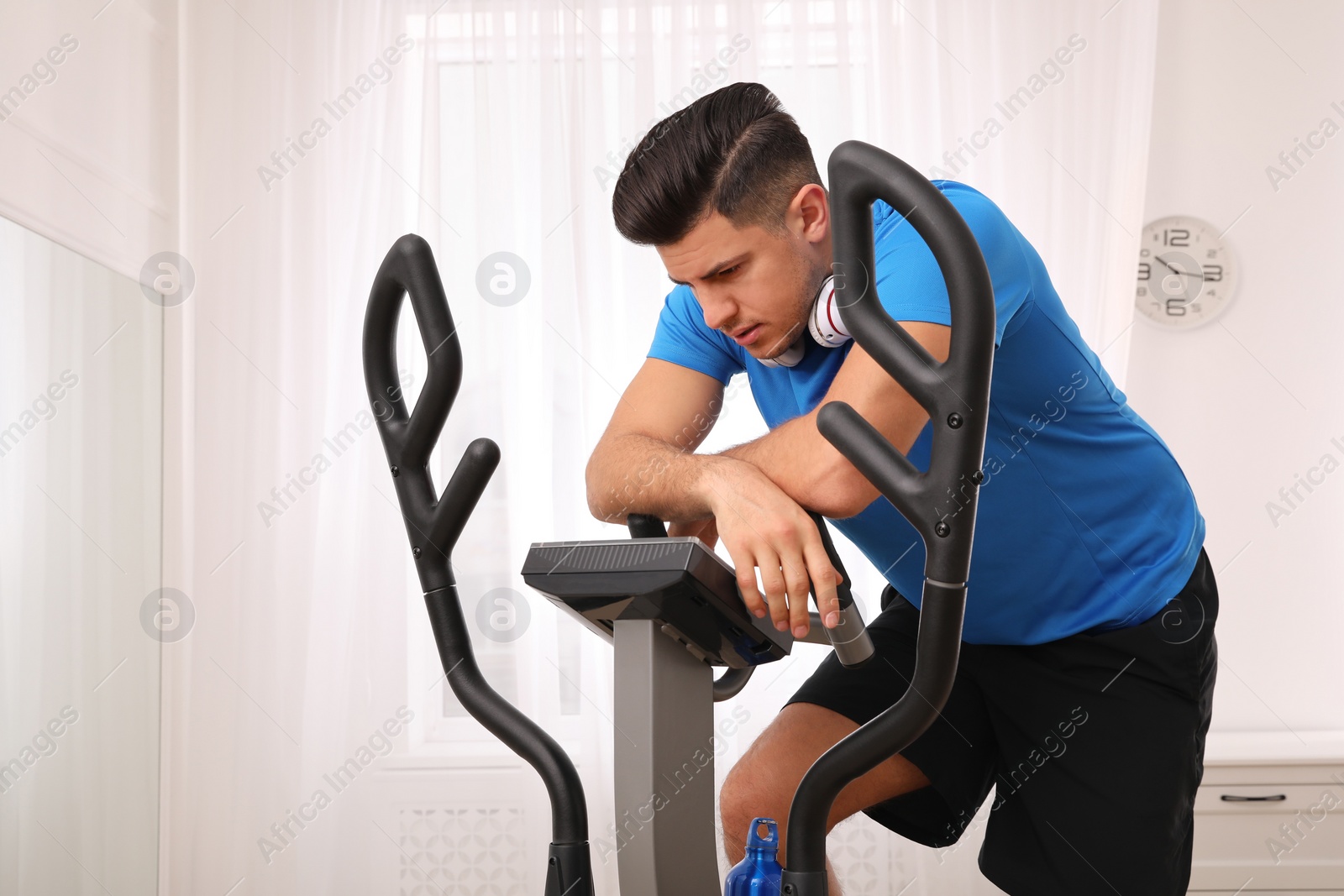Photo of Tired man after training on modern elliptical machine at home