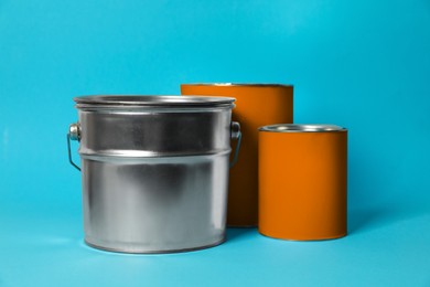 Photo of Cans and bucket of orange paint on turquoise background