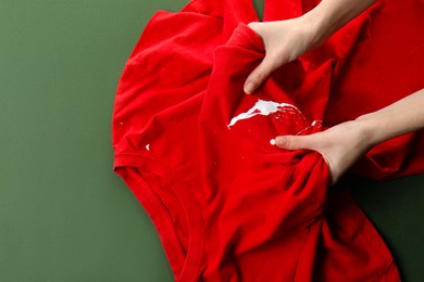 Woman holding red shirt with white paint stain on green background, top view. Space for text