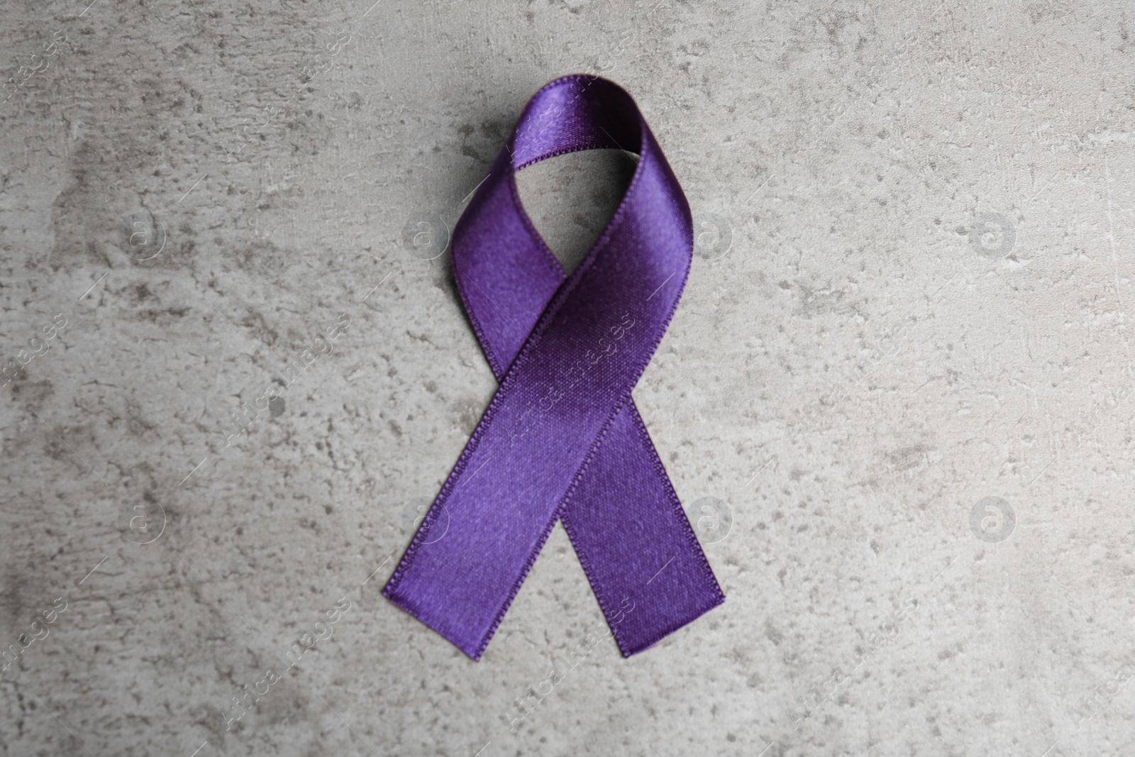 Photo of Purple ribbon on grey stone background, top view. Domestic violence awareness