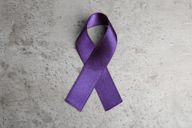 Purple ribbon on grey stone background, top view. Domestic violence awareness