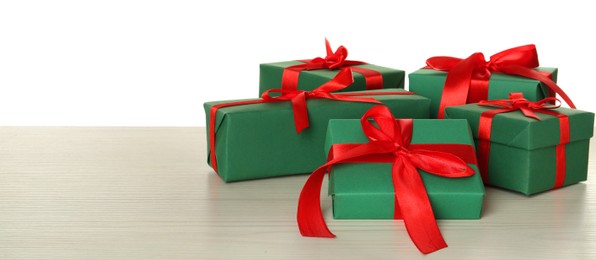 Photo of Green gift boxes with red bows on wooden table against white background, space for text
