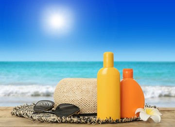 Image of Bottles of skin sun protection products and beach accessories on wooden table against seascape. Space for design