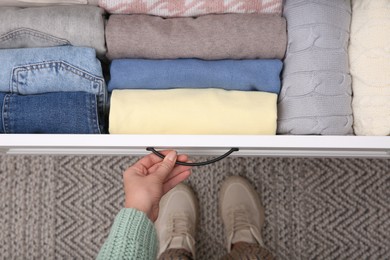 Photo of Woman opening drawer with folded clothes indoors, top view. Vertical storage