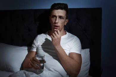 Photo of Young man with terrible headache taking pills in bed at night