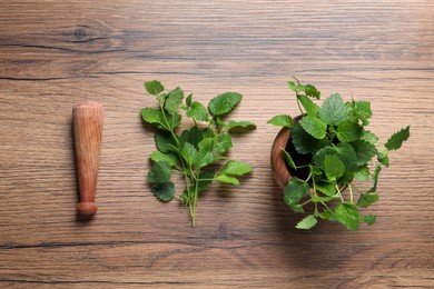 Photo of Mortar, pestle and fresh lemon balm on wooden table, flat lay