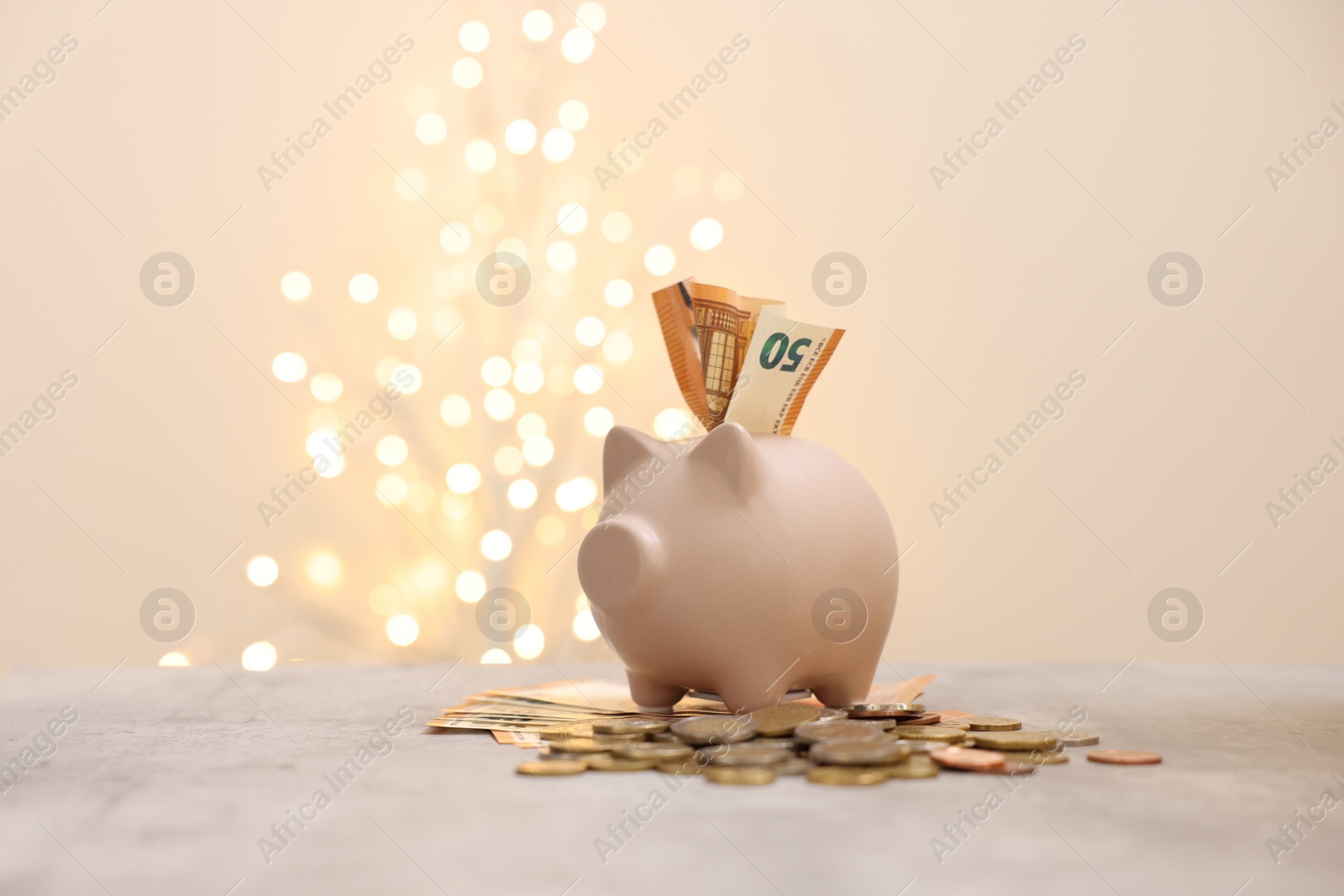 Photo of Piggy bank with euro banknote and coins on grey table against blurred lights, space for text