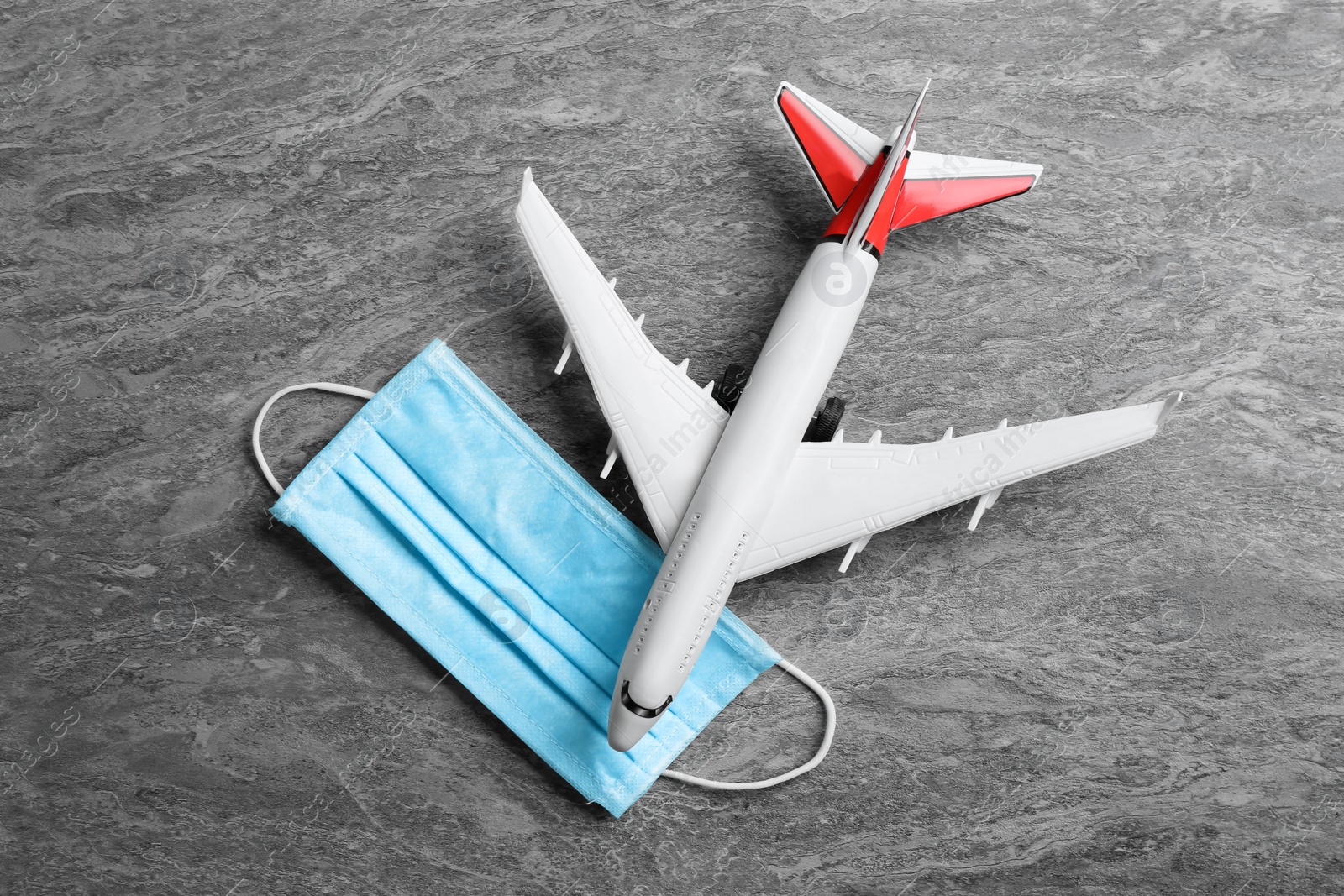 Photo of Toy airplane and medical mask on grey stone background, flat lay. Travelling during coronavirus pandemic