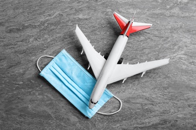 Toy airplane and medical mask on grey stone background, flat lay. Travelling during coronavirus pandemic