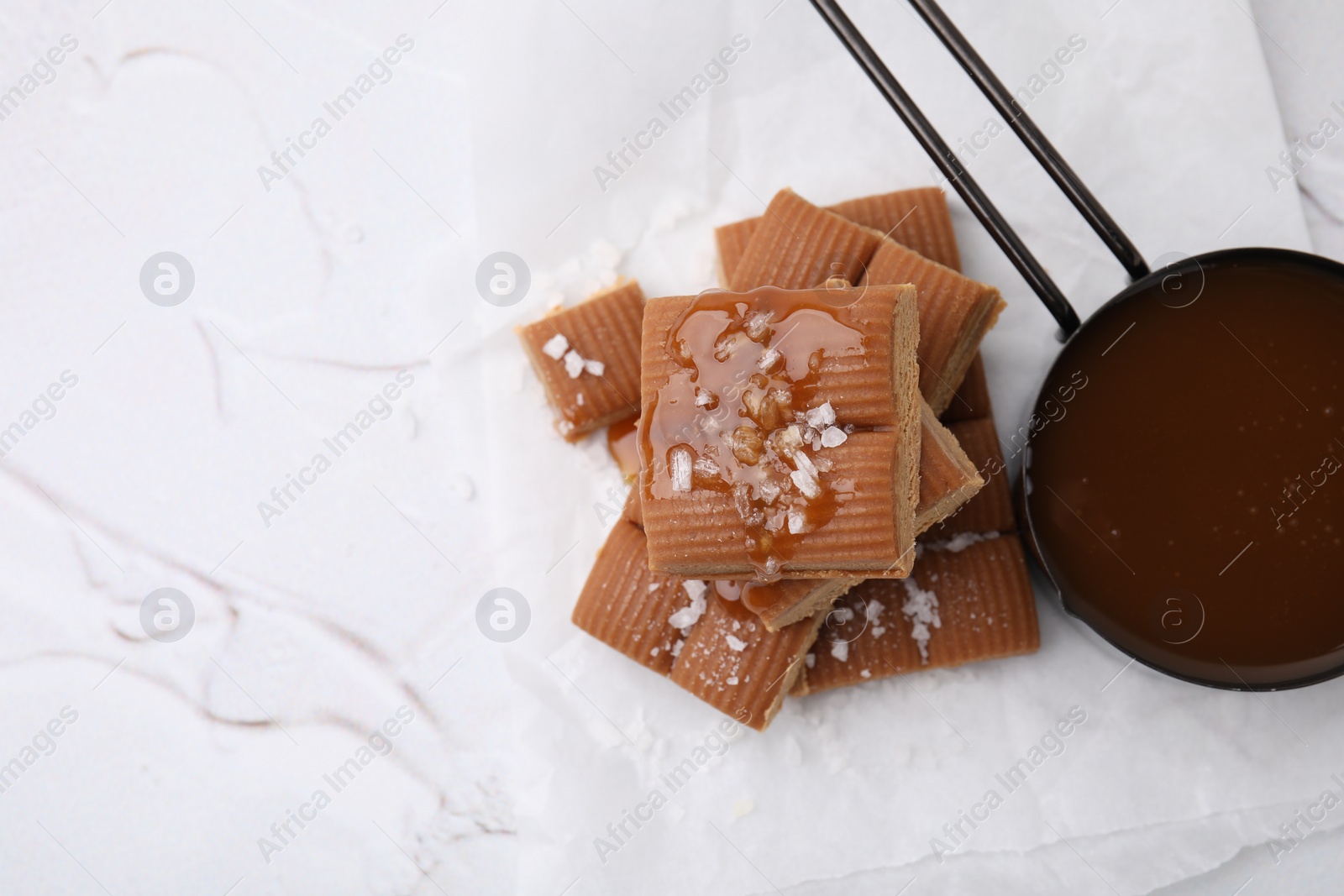 Photo of Yummy caramel candies, sauce and sea salt on white table, top view. Space for text