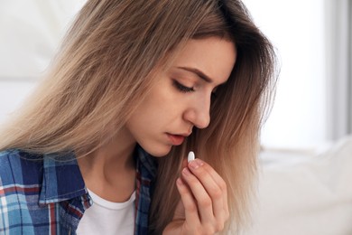 Photo of Upset young woman taking abortion pill on blurred background, closeup