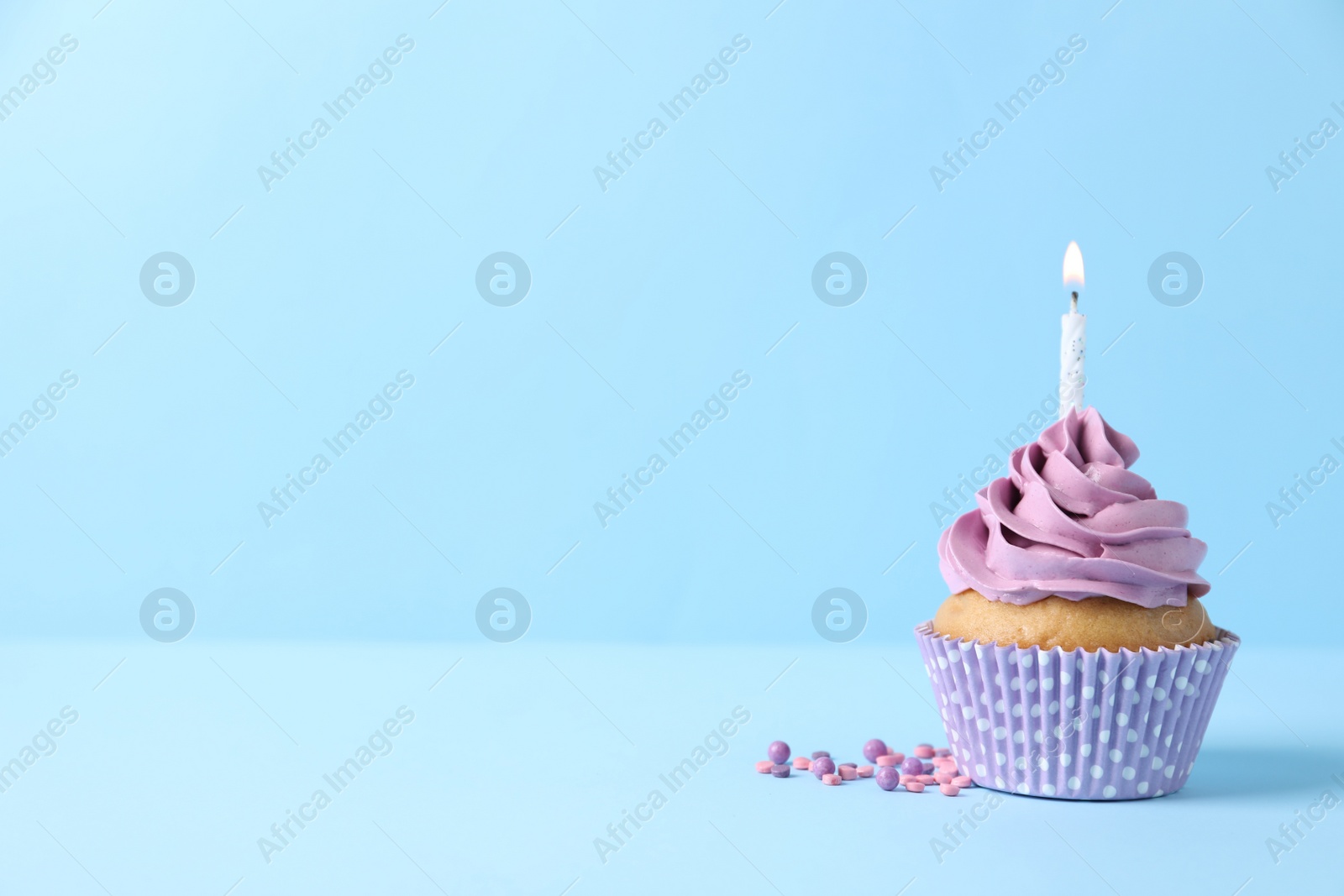Photo of Delicious birthday cupcake with burning candle and sprinkles on light blue background, space for text