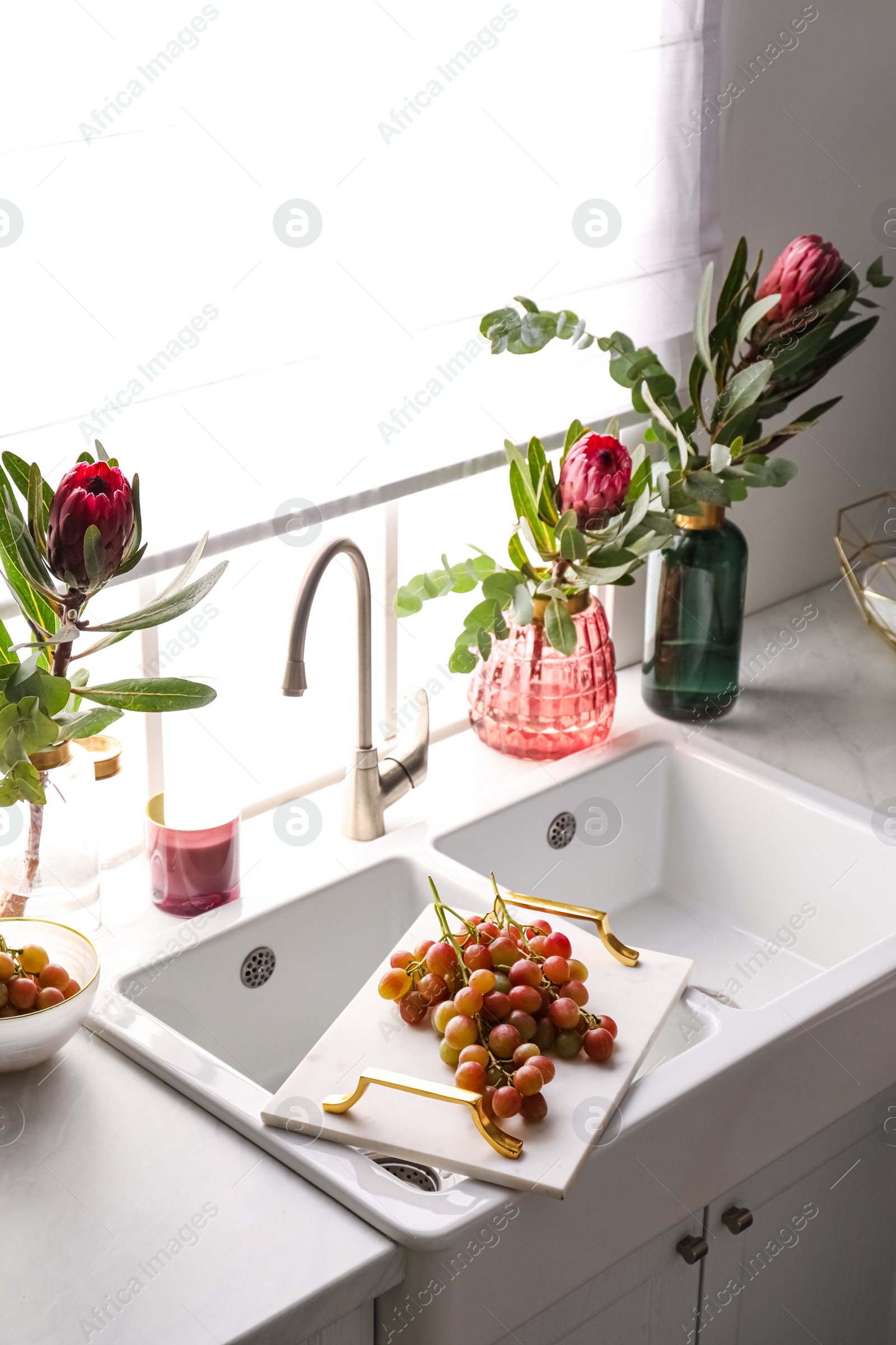 Photo of Vases with beautiful protea flowers near sink in kitchen. Interior design