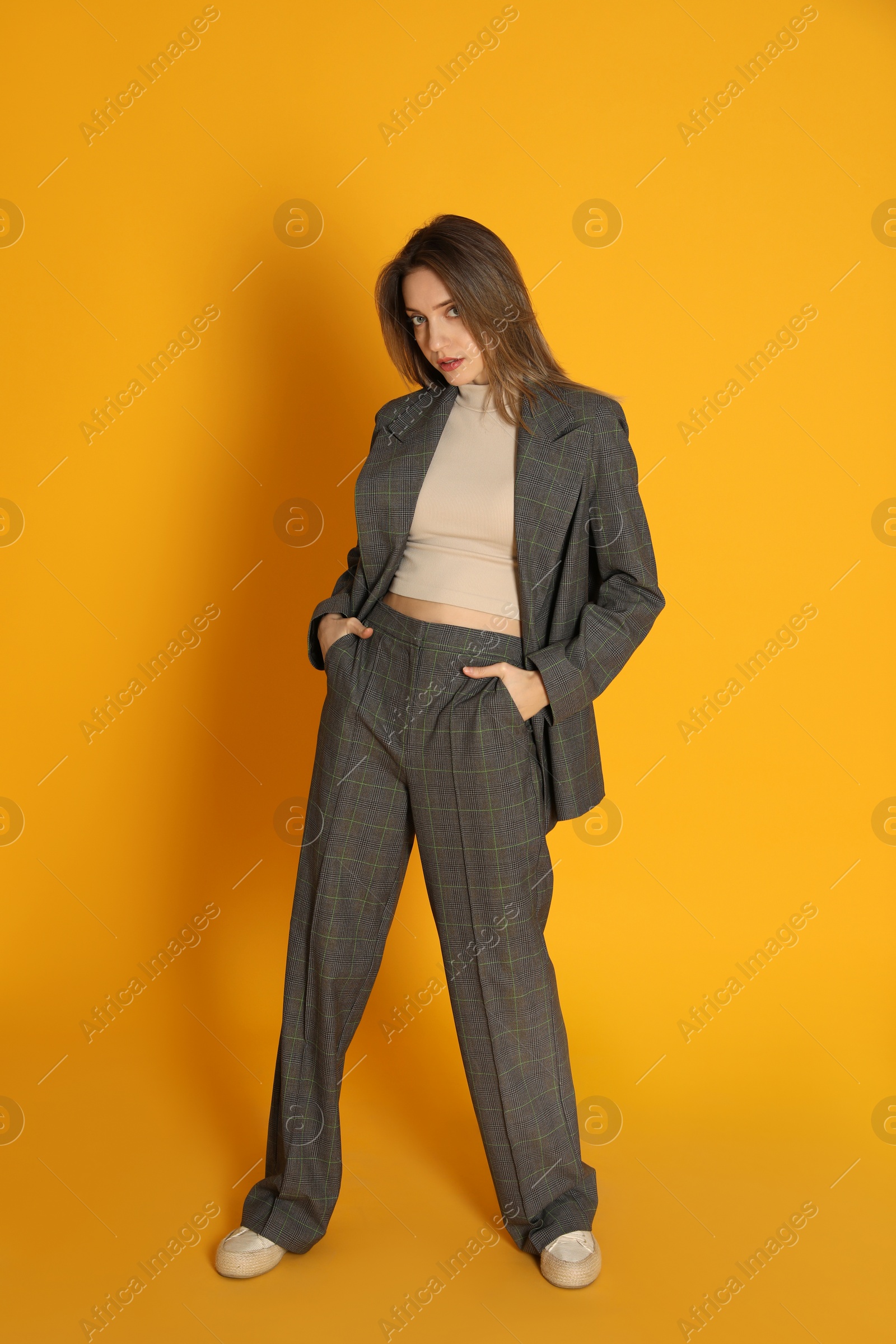 Photo of Full length portrait of beautiful young woman in fashionable suit on yellow background. Business attire