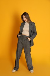 Full length portrait of beautiful young woman in fashionable suit on yellow background. Business attire