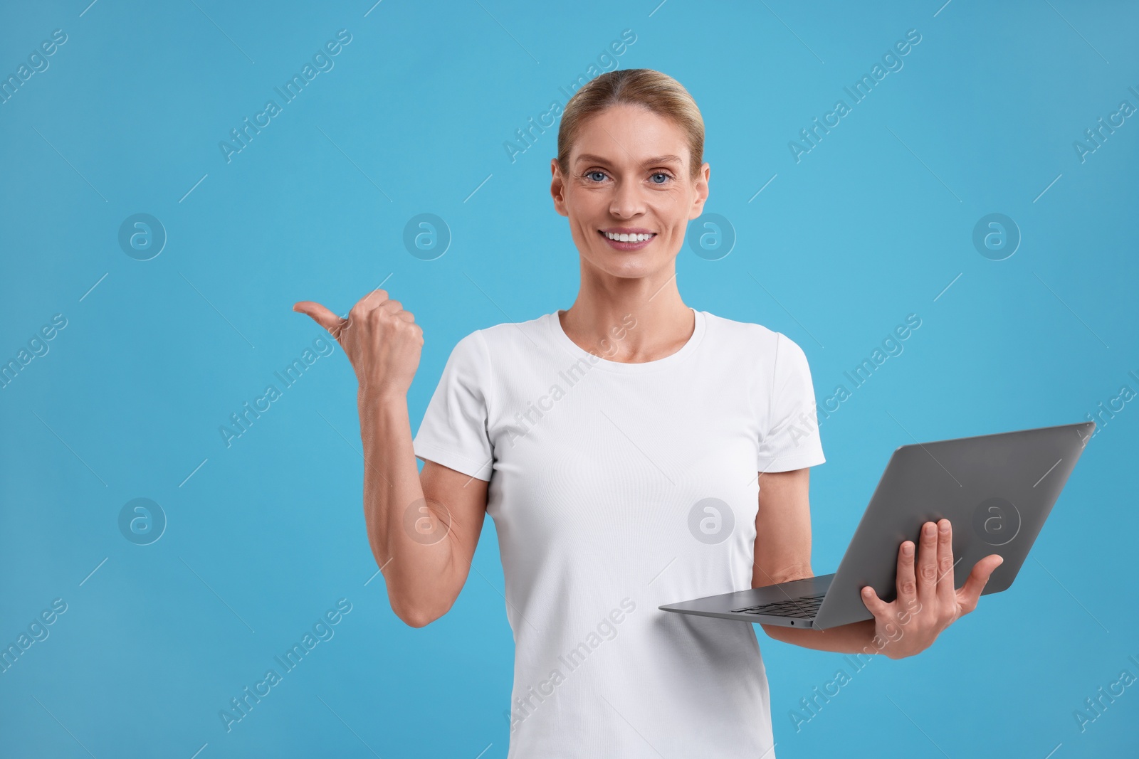 Photo of Special promotion. Smiling woman with laptop pointing at something on light blue background