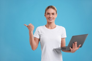 Special promotion. Smiling woman with laptop pointing at something on light blue background