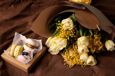 Photo of Bouquet of beautiful spring flowers and macarons on brown fabric