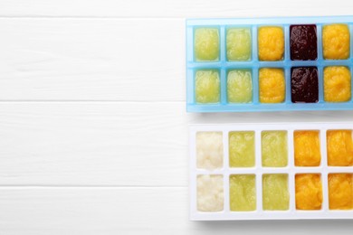 Photo of Different purees in ice cube trays ready for freezing on white wooden table, flat lay. Space for text