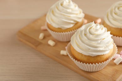 Photo of Delicious cupcakes with cream and marshmallows on wooden table, closeup. Space for text