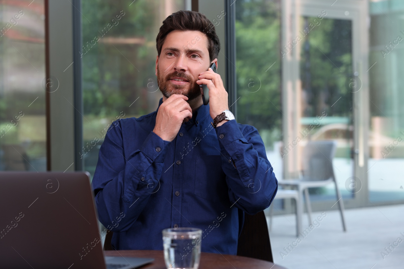 Photo of Handsome man talking on phone at table indoors