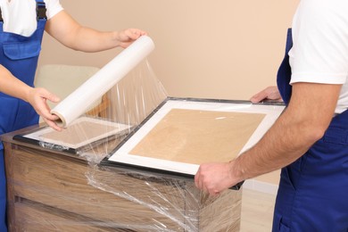 Workers wrapping picture frame in stretch film indoors, closeup