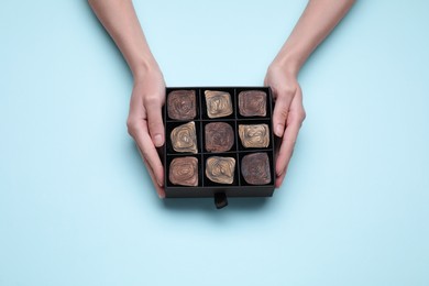 Photo of Woman with box of delicious chocolate candies on light blue background, top view