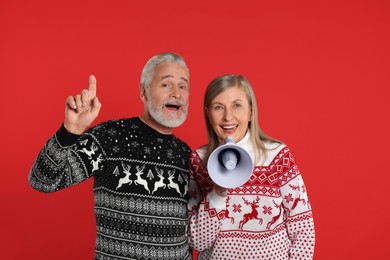 Photo of Senior couple in Christmas sweaters shouting in megaphone on red background