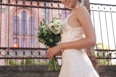 Photo of Gorgeous bride in beautiful wedding dress with bouquet near church, closeup
