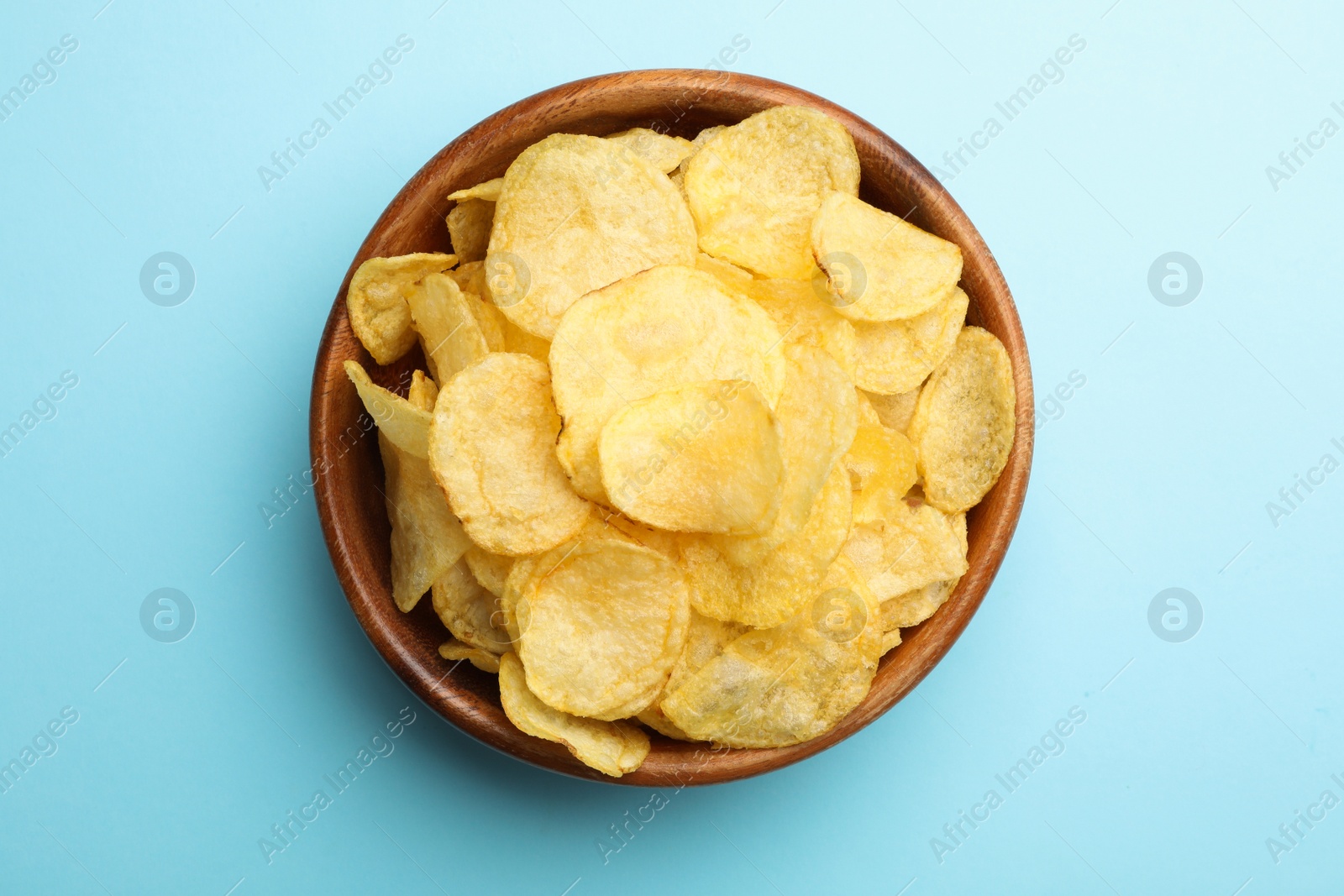 Photo of Delicious crispy potato chips in bowl on color background, top view