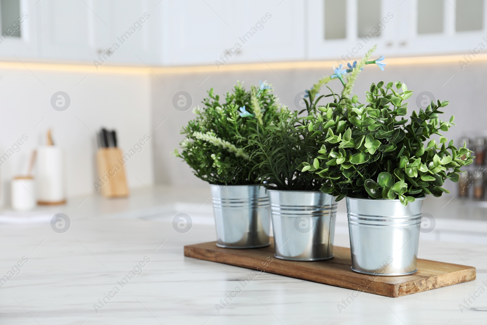 Photo of Different artificial potted herbs on white marble table in kitchen, space for text