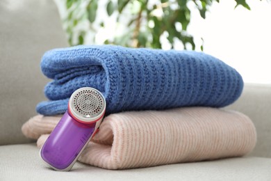 Photo of Modern fabric shaver and woolen sweaters on sofa indoors, closeup
