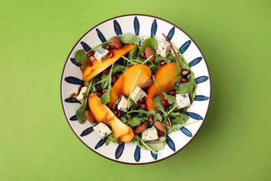 Photo of Tasty salad with persimmon, blue cheese, pomegranate and almonds served on light green background, top view