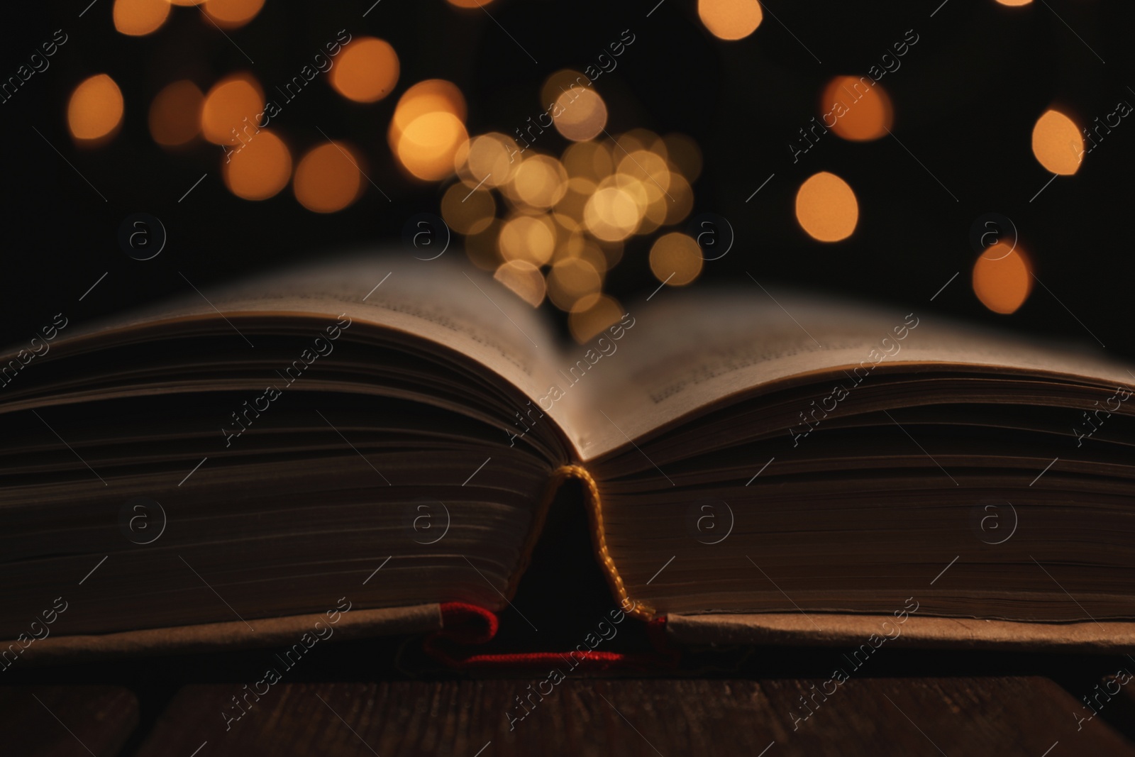 Photo of Open book and blurred lights on black background, closeup