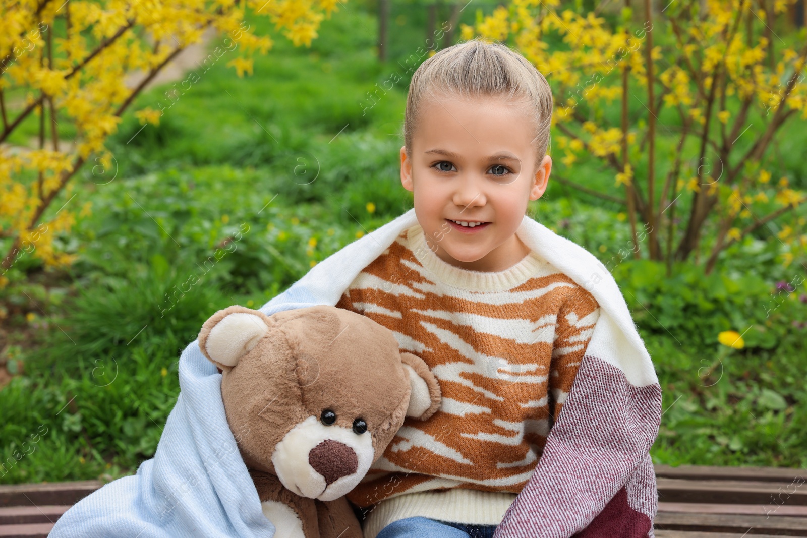 Photo of Little girl with teddy bear on wooden bench outdoors