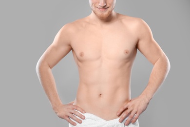 Photo of Young man with slim body in towel on grey background, closeup