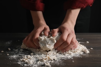 Making bread. Woman kneading dough at wooden table on dark background, closeup