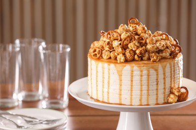 Photo of Caramel drip cake decorated with popcorn and pretzels near tableware on table