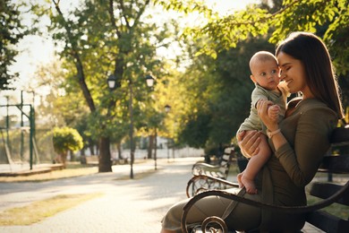 Photo of Young mother with her cute baby on bench in park