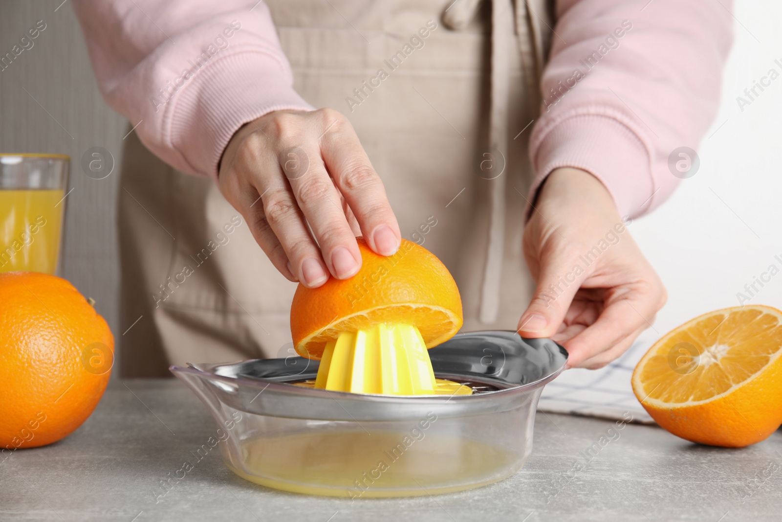 Photo of Woman squeezing orange juice at grey table, closeup