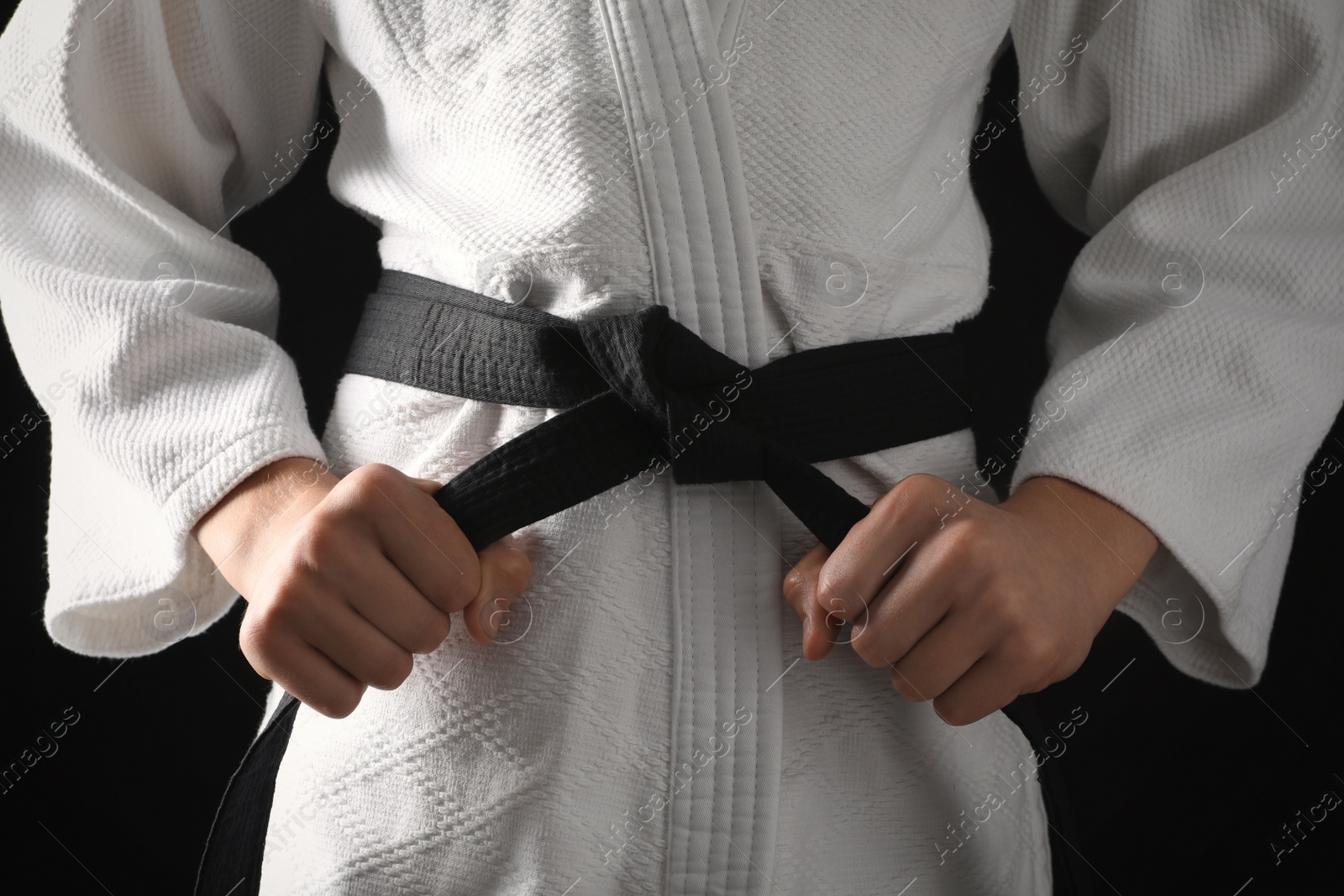 Photo of Man in keikogi with black belt on dark background, closeup. Martial arts uniform