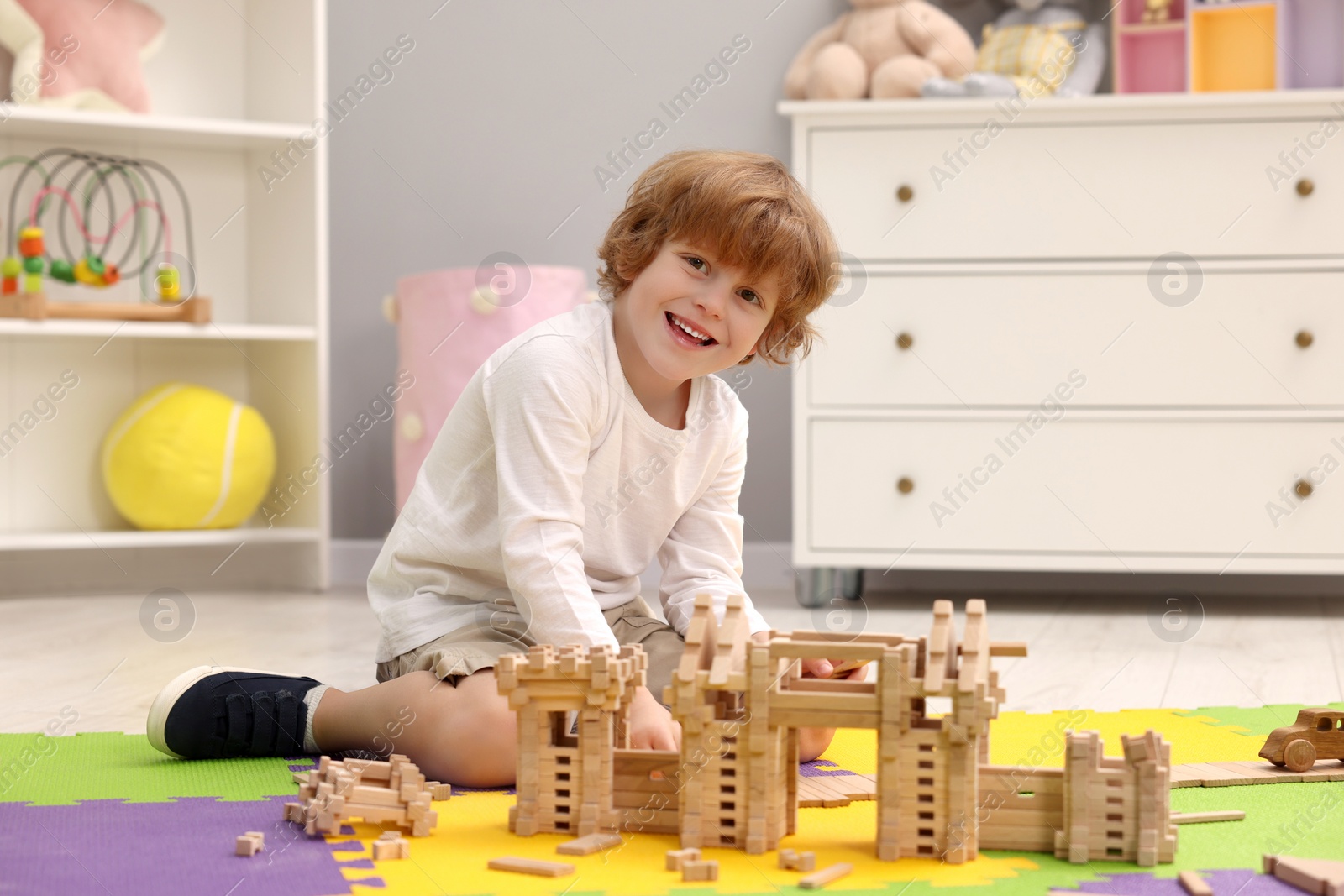 Photo of Little boy playing with wooden construction set on puzzle mat in room. Child's toy